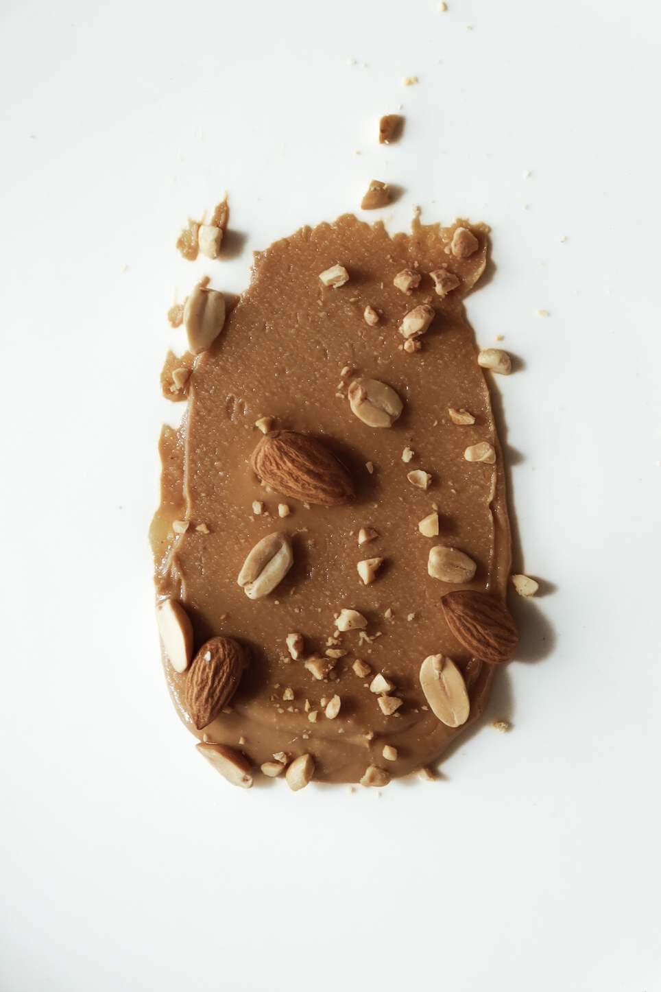 Mantequilla de almendra untada con almendras troceadas sobre fondo blanco